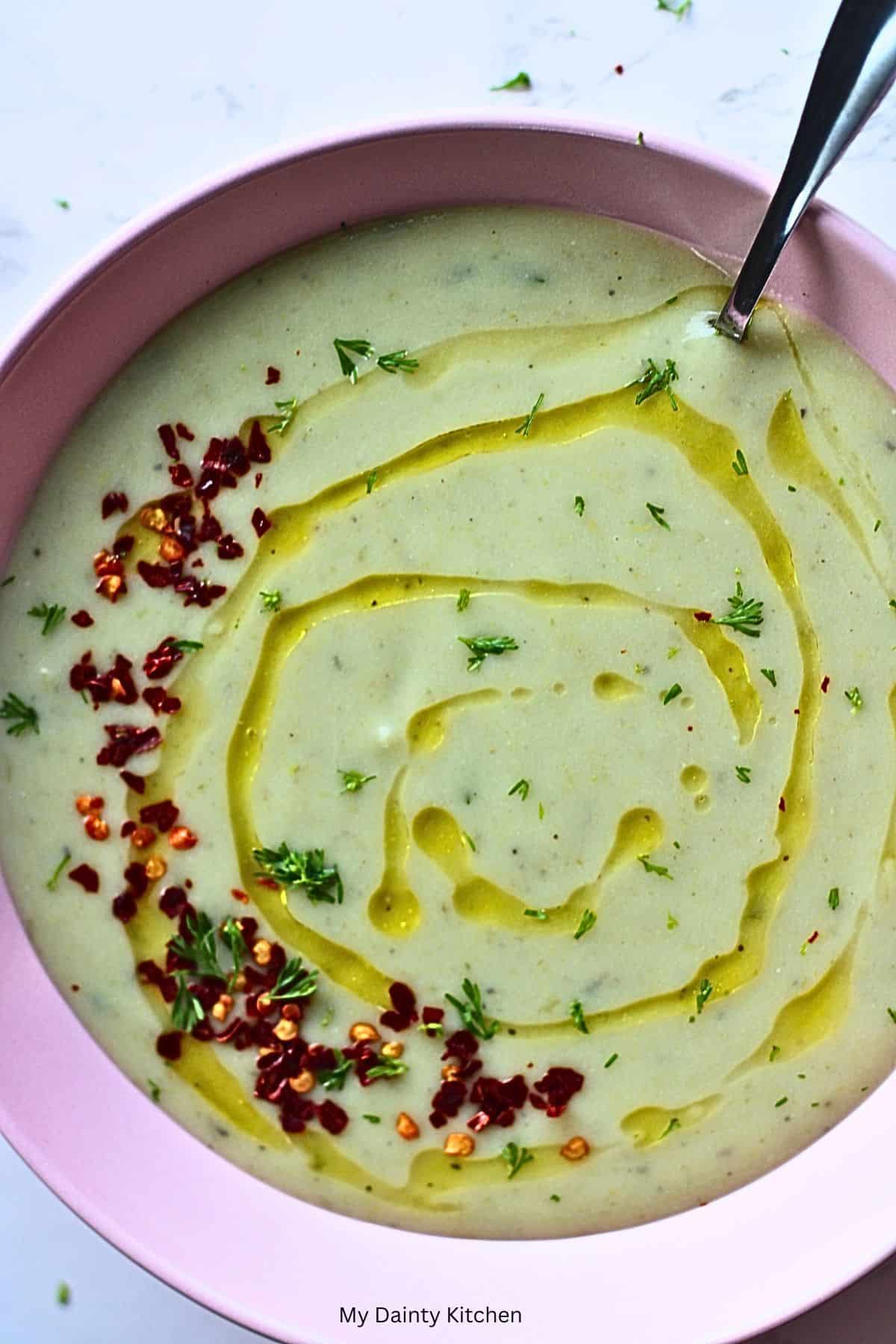 vegan zucchini soup in a bowl garnished with red pepper flakes, parsleys, and drizzle of olive oil